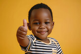 Happy little cute African boy giving thumbs up on yellow background