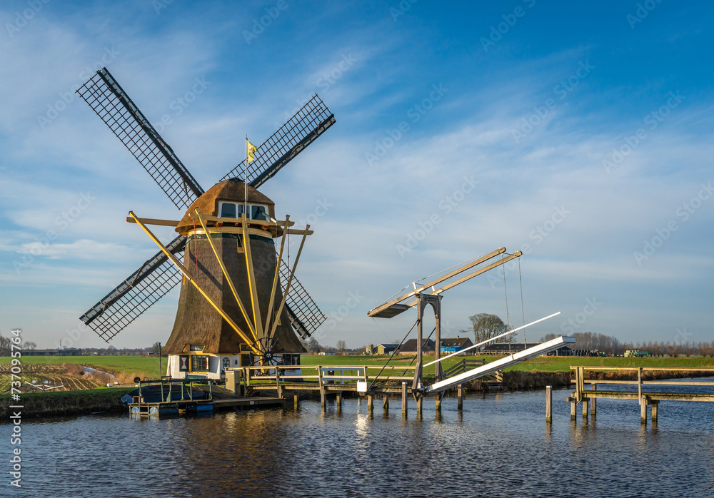 Scenery with wooden drawbridge and historical windmill in dutch village of Baambrugge