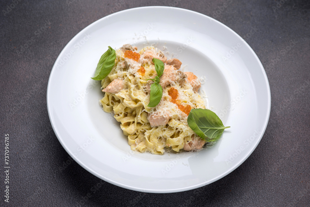 Pasta with salmon, cream sauce and basil on a white plate