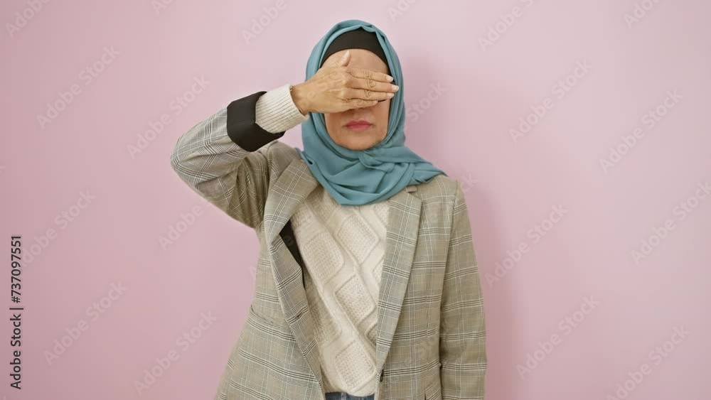 Mature, serious hispanic woman in hijab, blindly covering eyes with hand - a sad reflection of rejection, hiding behind her veil over isolated pink background Mature, serious hispanic woman in hijab, blindly covering eyes with hand - a sad reflection of rejection, hiding behind her veil over isolated pink background