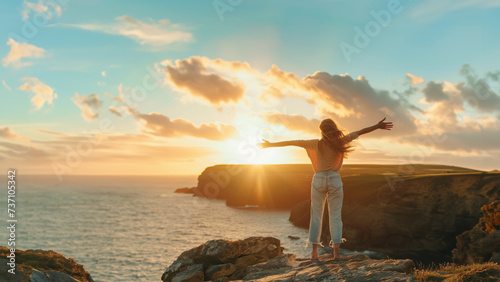 A woman standing at the top of a cliff, open arms enjoying beautiful landscape with sunset during summer. Enjoying the sensation of freedom during holidays or vacation in exotic traveling destination