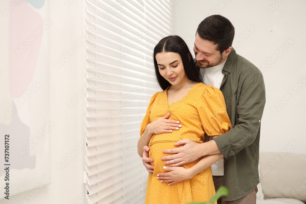 Pregnant woman with her husband indoors, space for text
