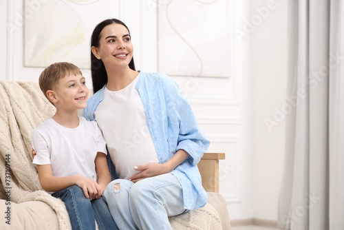 Happy pregnant woman with her son on sofa at home, space for text