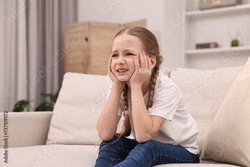 Little girl suffering from headache on sofa indoors