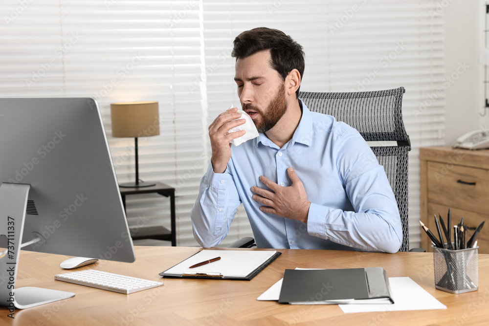 Sick man with tissue coughing at workplace in office