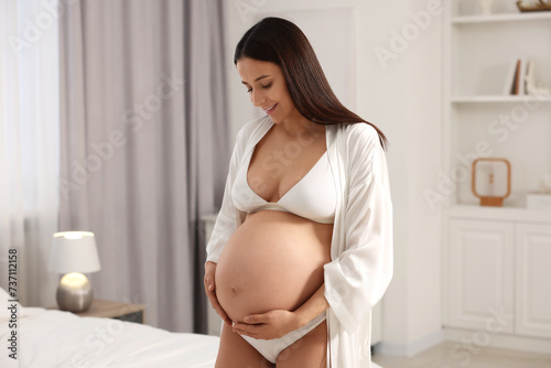 Beautiful pregnant woman wearing stylish comfortable underwear and robe in bedroom