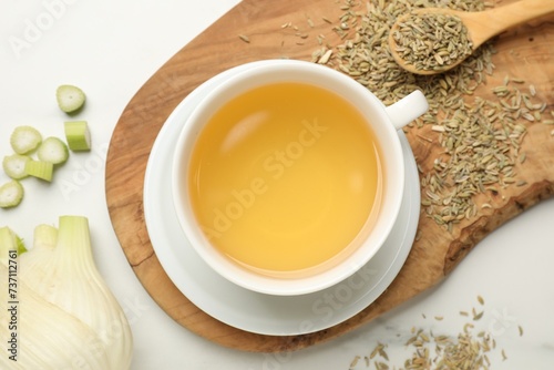 Fennel tea in cup, seeds and fresh vegetable on white marble table, flat lay