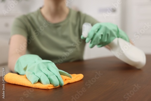 Woman with spray bottle and microfiber cloth cleaning wooden table in room, closeup © New Africa