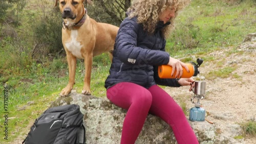 Curly and blonde hair, mountaineer woman and her dog camps and making tea with a gas stove