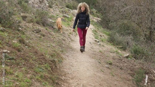 Curly and blonde hair, mountaineer woman and her dog walking through the mountains.
