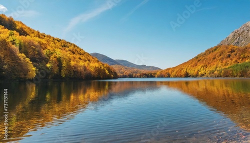calm nature scenery by the lake forest in bright fall colors on the shore covered in yellow foliage mountainous landscape on a sunny day reflecting on the water surface © Marsha