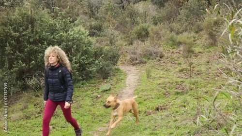 Curly and blonde hair, mountaineer woman and her dog walking through the mountains.