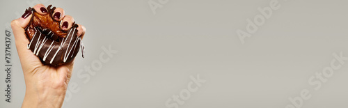 unknown woman with nail polish squeezing sweet donut with brown icing on gray background, banner