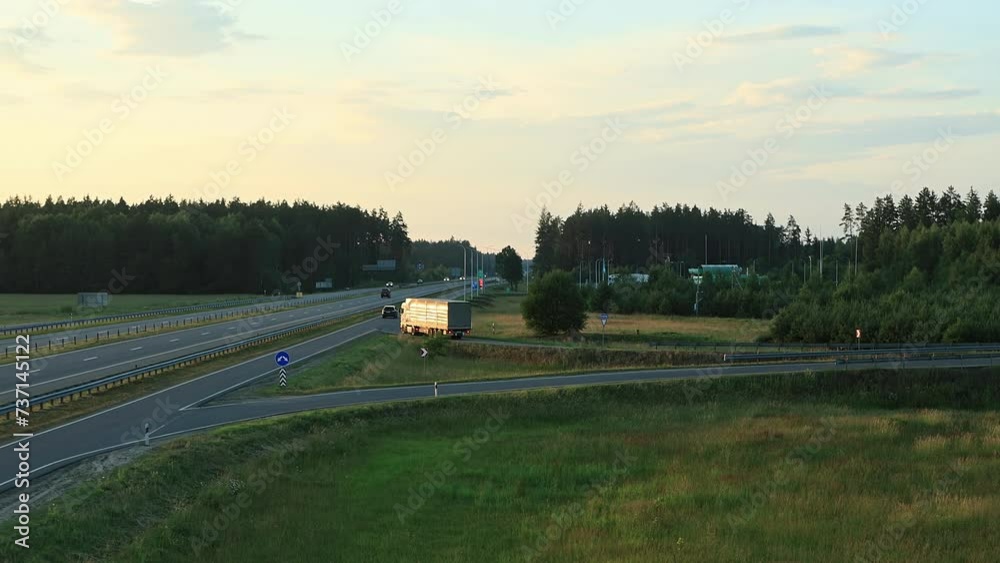 Tautliner A-frame drawbar full trailer truck with curtain side drives off bridge and onto highway at sunset tonight. Export import by semi-trailer, logistic company. Freight transit delivery Tautliner A-frame drawbar full trailer truck with curtain side drives off bridge and onto highway at sunset tonight. Export import by semi-trailer, logistic company. Freight transit delivery