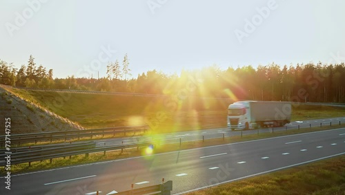 A-frame drawbar full curtainside trucks driving on highway under overpass in countryside at sunset. Cargo lory semi-trailers move on road under flyover overbridge. Export import, delivery logistic photo