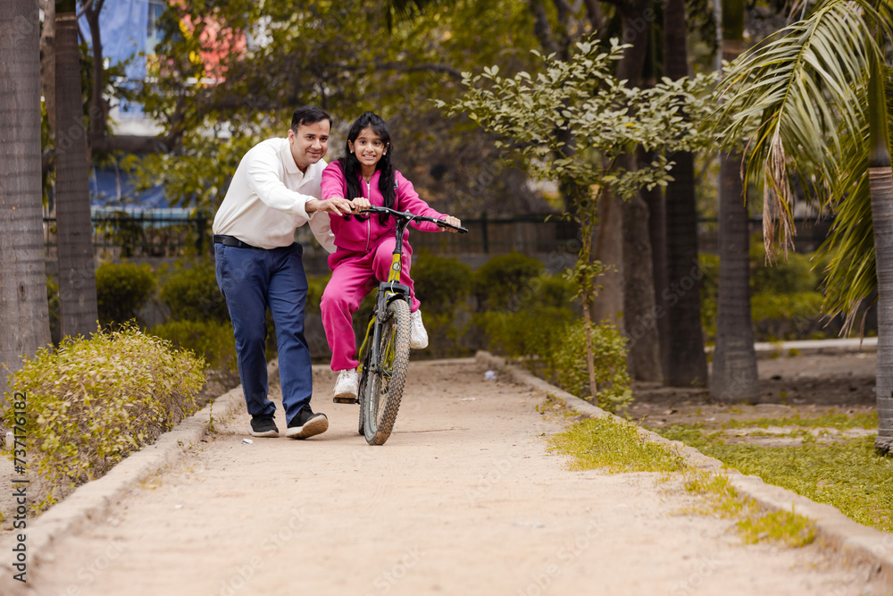 Obraz premium Indian Latin Father helping Daughter With cycling in Outdoor Garden