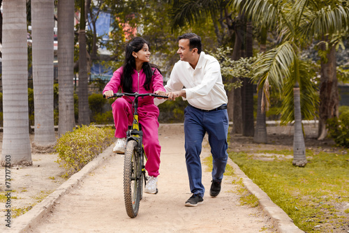 Indian Latin Father helping Daughter With cycling in Outdoor Garden © Photographielove