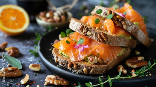 a black plate topped with slices of bread covered in toppings and nuts next to an orange slice of fruit.