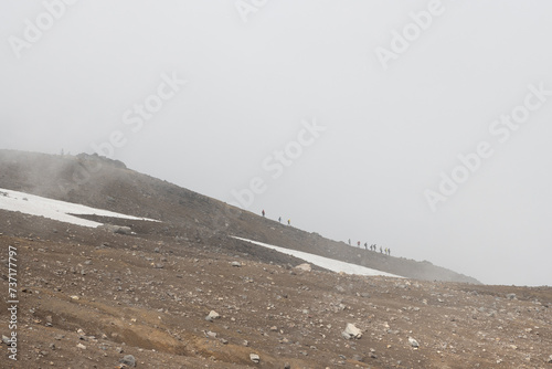 Foggy mountain landscape. Hikers go down the slope of the volcano. Low clouds, fog and poor visibility. Travel, tourism and hiking on the Kamchatka Peninsula. Gorely volcano, Kamchatka Krai, Russia. photo