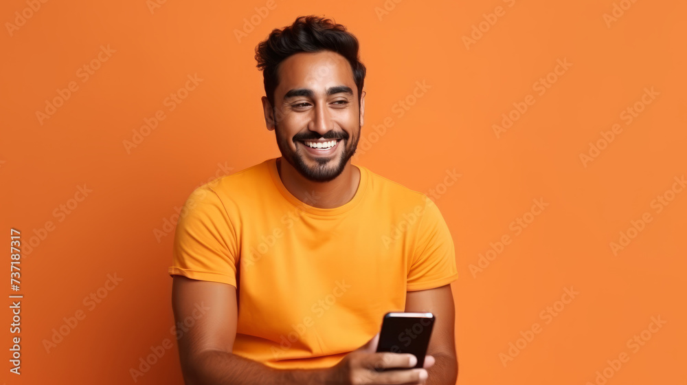 Smiling young man in yellow shirt holding smartphone against orange background Smiling young man in yellow shirt holding smartphone against orange background