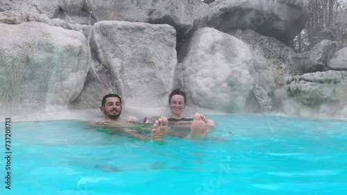 Renewal vitality and energy procedures in thermal hot water baths under the open air, friends smiling and waving feet on camera lying in water, geothermal spring with sulphur vapours. Healing benefits
