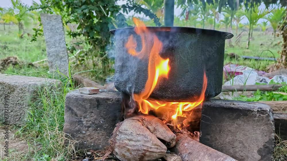 Heating water in black rustic vessel by burning plastic, coconut husk, and wood in a brick stove Heating water in black rustic vessel by burning plastic, coconut husk, and wood in a brick stove