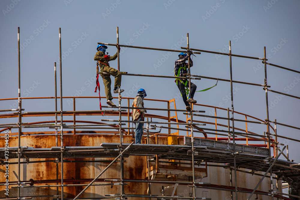 Fototapeta premium Construction workers installing scaffolding storage tank Oil​ refinery​ and​ plant and tower column
