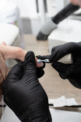 Beauty concept. A manicurist in black latex gloves makes a hygienic manicure and paints the client s nails with gel polish in a beauty salon. Close-up.