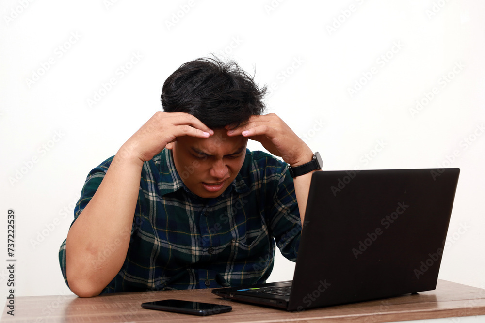Stressed young asian man sitting while using a laptop Stressed young asian man sitting while using a laptop