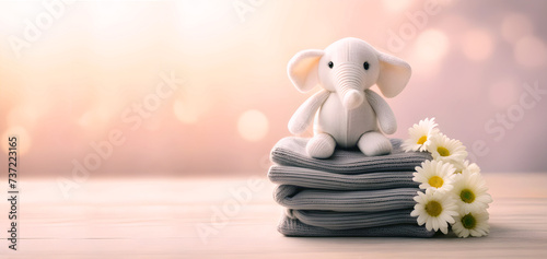 Muñeco de elefante sentado sobre ropa de lana. Pila de ropa de lana con peluche encima y flores decorando. IA.
