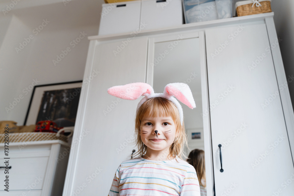 Smiling little girl with painted face and wearing bunny ears on Easter day. Preschool children spending time at home or daycare Smiling little girl with painted face and wearing bunny ears on Easter day. Preschool children spending time at home or daycare