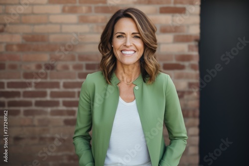 Portrait of smiling businesswoman in green jacket standing against brick wall