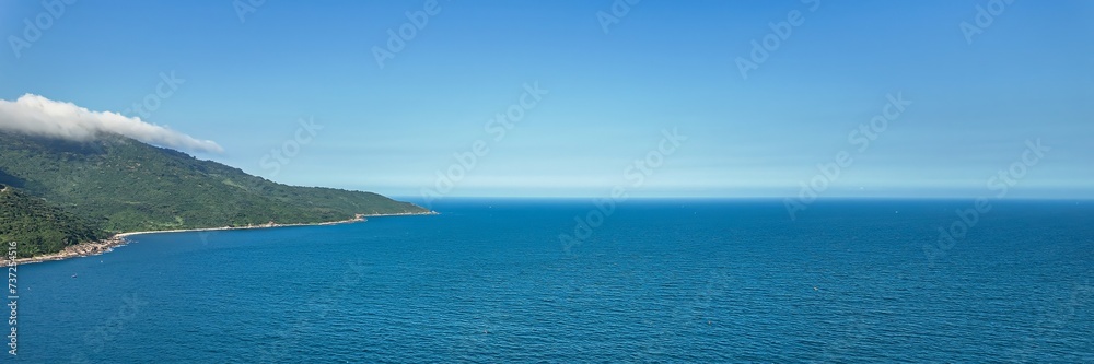 Breathtaking panoramic aerial view of a lush green coastal landscape meeting the calm blue sea under a clear sky, symbolizing tranquility and natural beauty