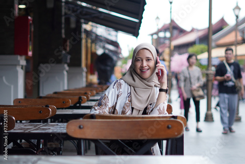 Indonesian Woman wearing Hijab Engaging in Digital Conversations at Cafe Bench photo