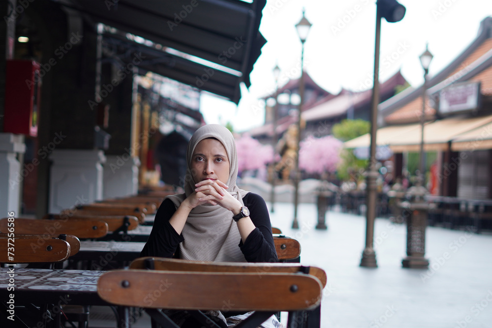Fototapeta premium Serene Contemplation concept. Indonesian Hijabi Woman Lost in Thought at Cafe Bench