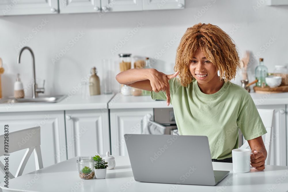 cheerful african american woman using sign language during video call and holding cup of coffee cheerful african american woman using sign language during video call and holding cup of coffee