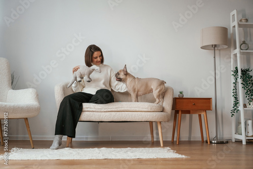 Front view, sitting on the little sofa. Young woman is with her pug dog at home #737260912