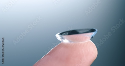 Super slow motion of drop of liquid solution for clean and disinfect is falling on contact eye ophthalmology optometry care optical lens kept on finger isolated on soft background at 1000 fps. photo