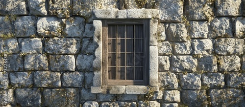 A stone wall with a barred window is a sturdy building fixture that adds character to the brickwork facade of the house