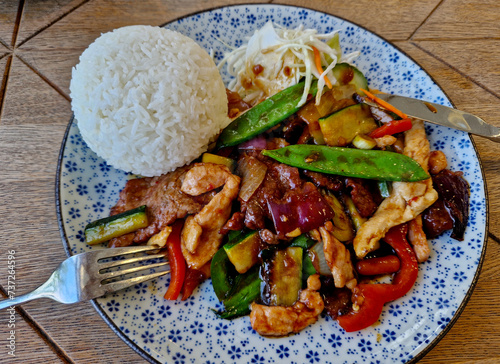 Szechuan style chicken with roasted meat and green pea pods and a mound of rice. flower plate, cabbage salad and paprika. colorful healthy food in a Vietnamese style with a view photo