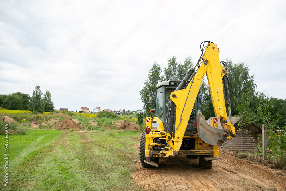 A tractor levelling and clearing the construction site. Bulldozer earth work. Working process at a the back yard. Fence building. Tractor bucket close up. Moving the ground. Copy space. Back view A tractor levelling and clearing the construction site. Bulldozer earth work. Working process at a the back yard. Fence building. Tractor bucket close up. Moving the ground. Copy space. Back view