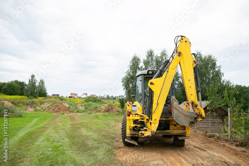 A tractor levelling and clearing the construction site. Bulldozer earth work. Working process at a the back yard. Fence building. Tractor bucket close up. Moving the ground. Copy space. Back view