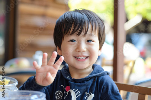 cute asian baby boy smiling and showing ok hand sign in restaurant
