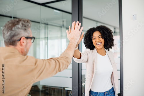 The colleagues exchange a high-five, their smiles reflecting a culture of achievement and mutual respect in a bright, modern office setting. The action signifies a successful collaboration
