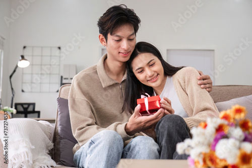 A young Asian couple gives each other gifts on their anniversary and sits happily together in the living room.