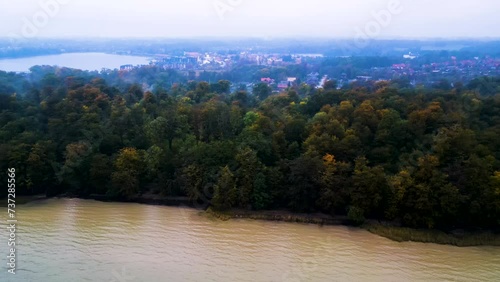 Herbstliche Flusslandschaft mit dichtem Wald und einer Kleinstadt im Hintergrund bei Morgendämmerung. Drohnenaufnahme Parallelfahrt. Fiskenæsvej, Graasten, Dänemark photo