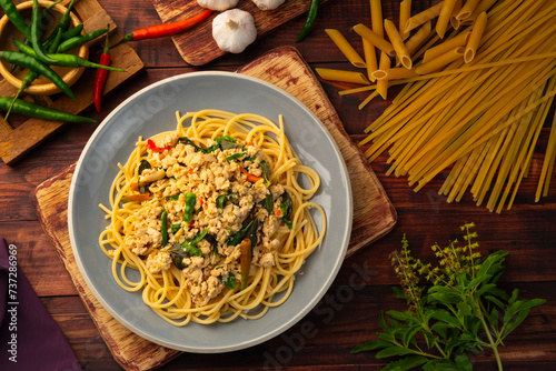 Stir fried spicy spaghetti with minced chicken breast and basil leaves in white plate,Spicy pasta Pad Kra Pao.Healthy Thai fusion food.Top view photo