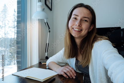 portrait photo of a woman at her desk. Personal view of young ukrainian woman working from home, waving and talking to camera, video conference with her business partners on laptop at home, videoblog