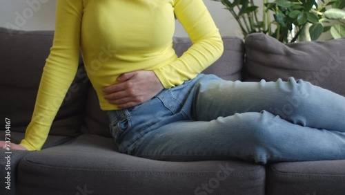 Close up of young woman holding belly, feeling discomfort, health problem concept, girl sit on sofa at home, suffering from stomach ache, food poisoning, gastritis, abdominal pain, menstrual period photo