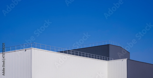 Modern white and black aluminium corrugated factory buildings with steel fence on rooftop against blue sky background in panoramic view photo